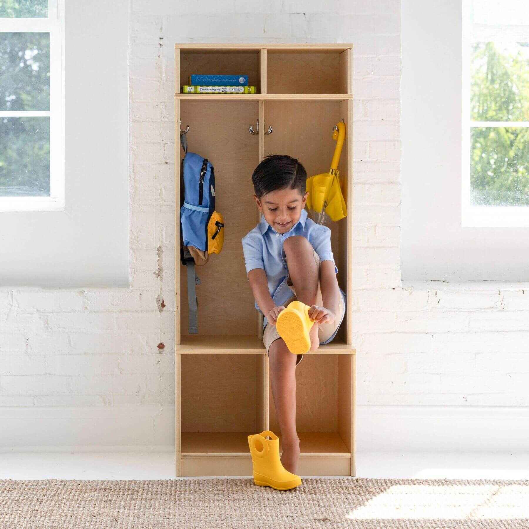 Child sitting inside Little Partners Learn 'N Store Cubby Natural, wearing yellow boots and holding a yellow toy.