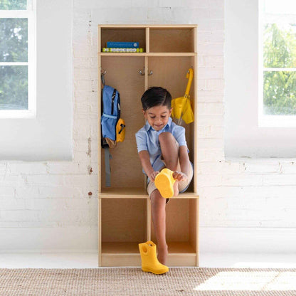 Child sitting inside Little Partners Learn 'N Store Cubby Natural, wearing yellow boots and holding a yellow toy.