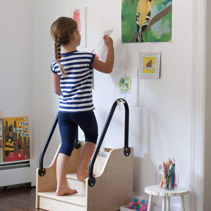 Child using a Little Partners ReachUp Step Stool to reach artwork on a wall