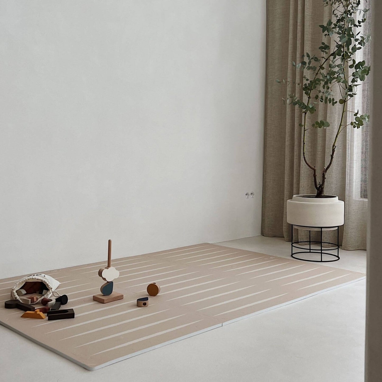 Eeveve Lucio Play Mat - Desert Sand, styled in a minimalist room corner with small toys, a potted plant, curtains, and a light wall.