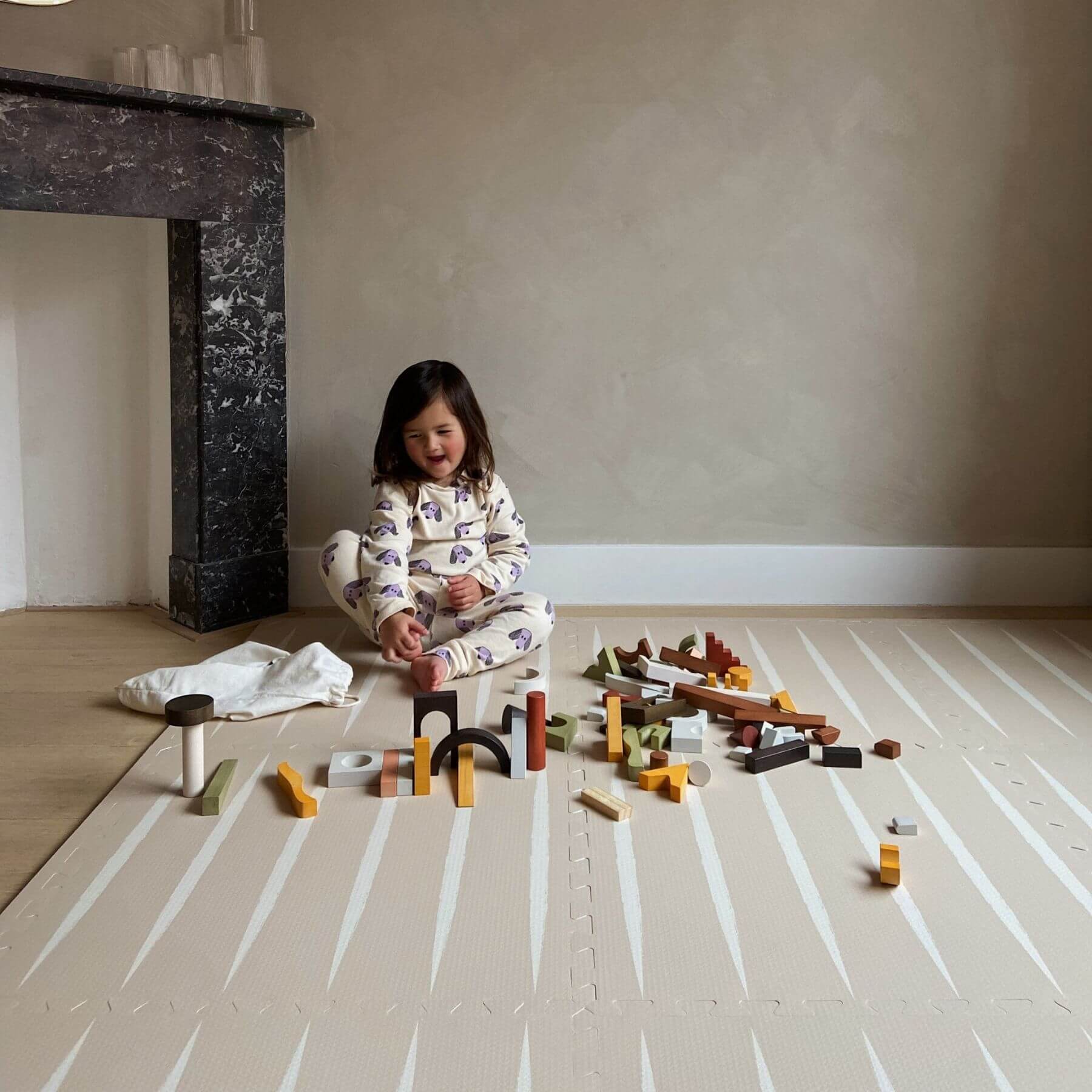 Child playing with building blocks on Eeveve Lucio Play Mat - Desert Sand in a room with a fireplace.