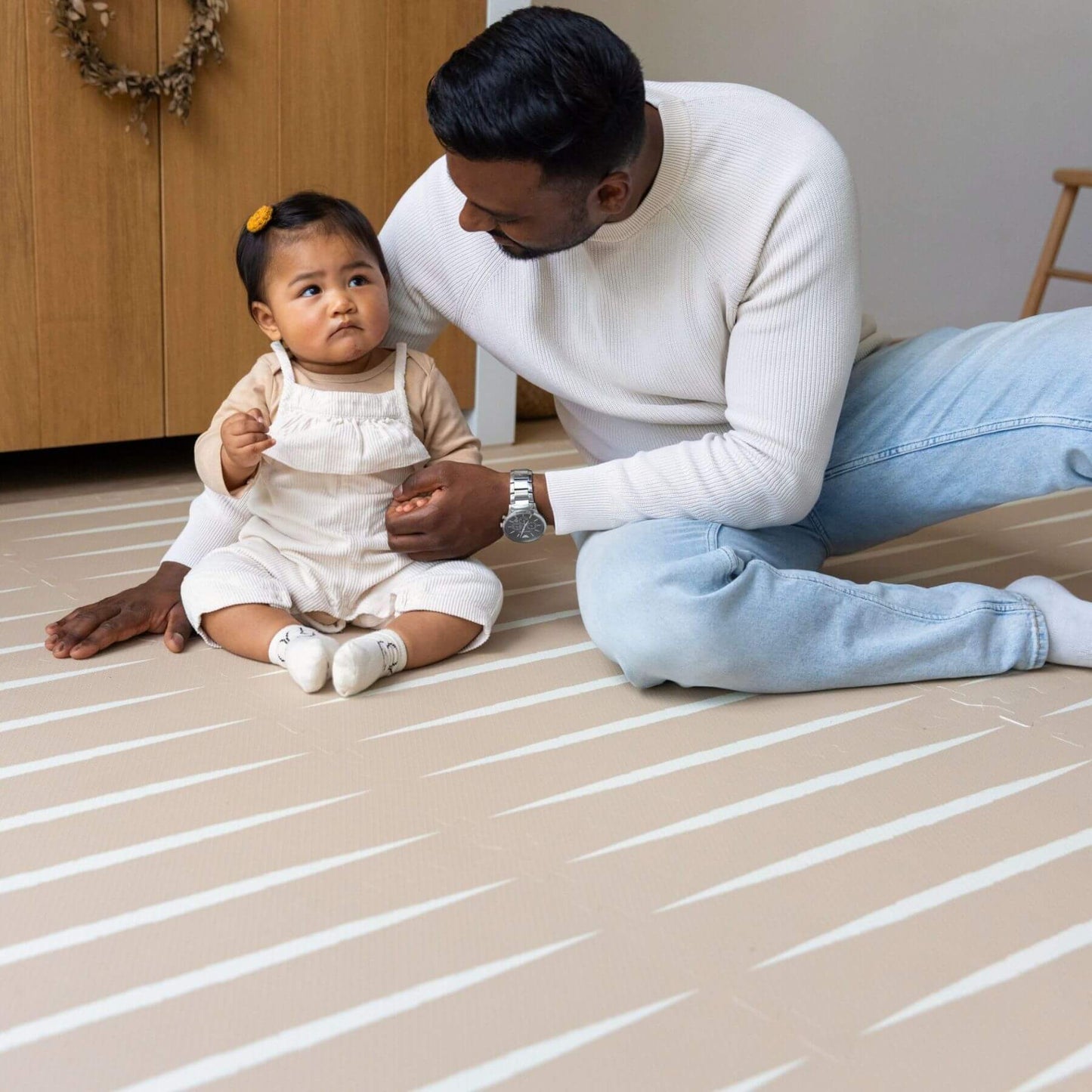 A man and a baby sitting on Eeveve Lucio Play Mat - Desert Sand in a home setting.