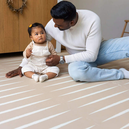 A man and a baby sitting on Eeveve Lucio Play Mat - Desert Sand in a home setting.