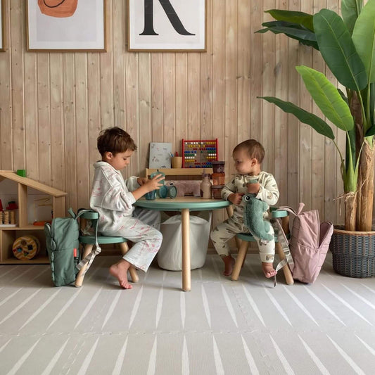 Two children playing at a small table in a room with wooden walls and a plant.