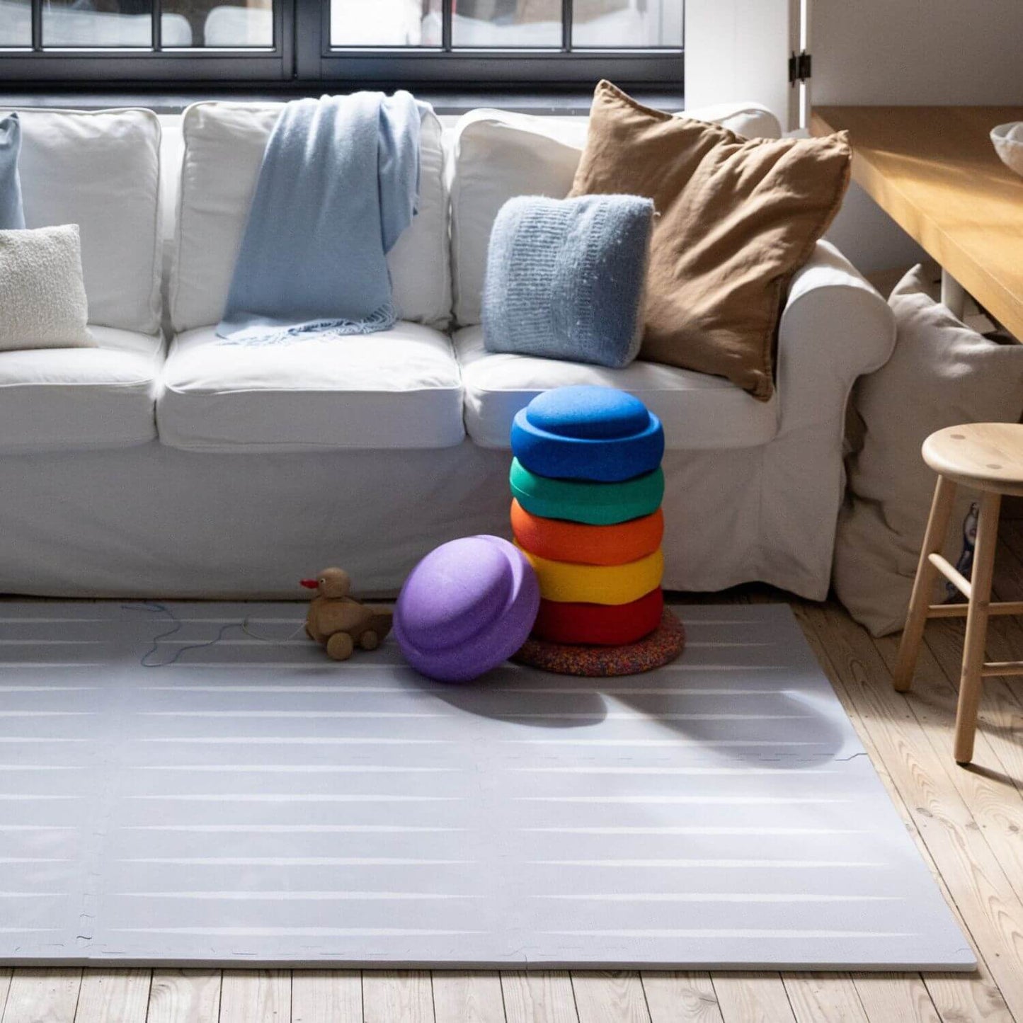 White sofa with colorful cushions and Lucio Play Mat Nordic Mist in a living room setting
