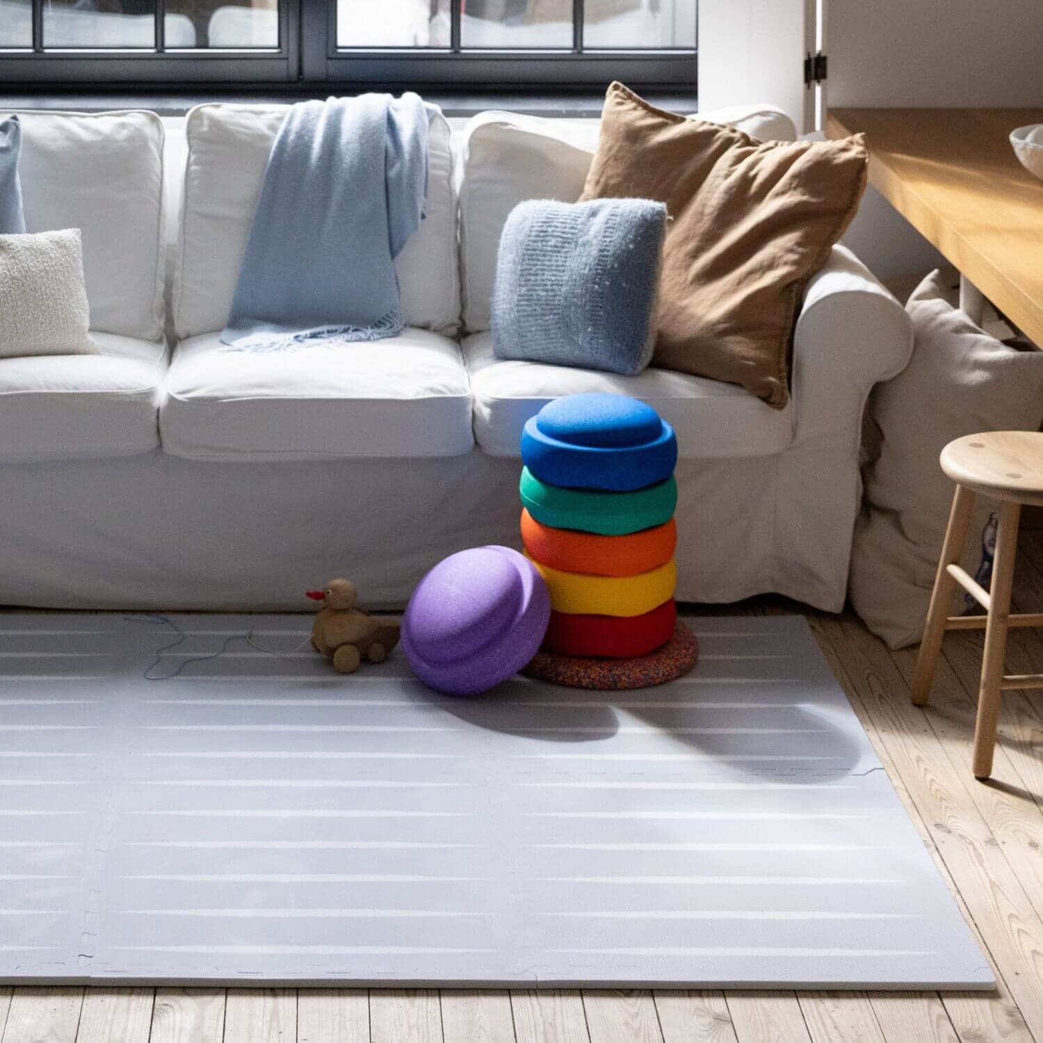 White sofa with colorful cushions and Lucio Play Mat Nordic Mist in a living room setting
