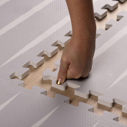 Hand placing play mat pieces on a wooden floor