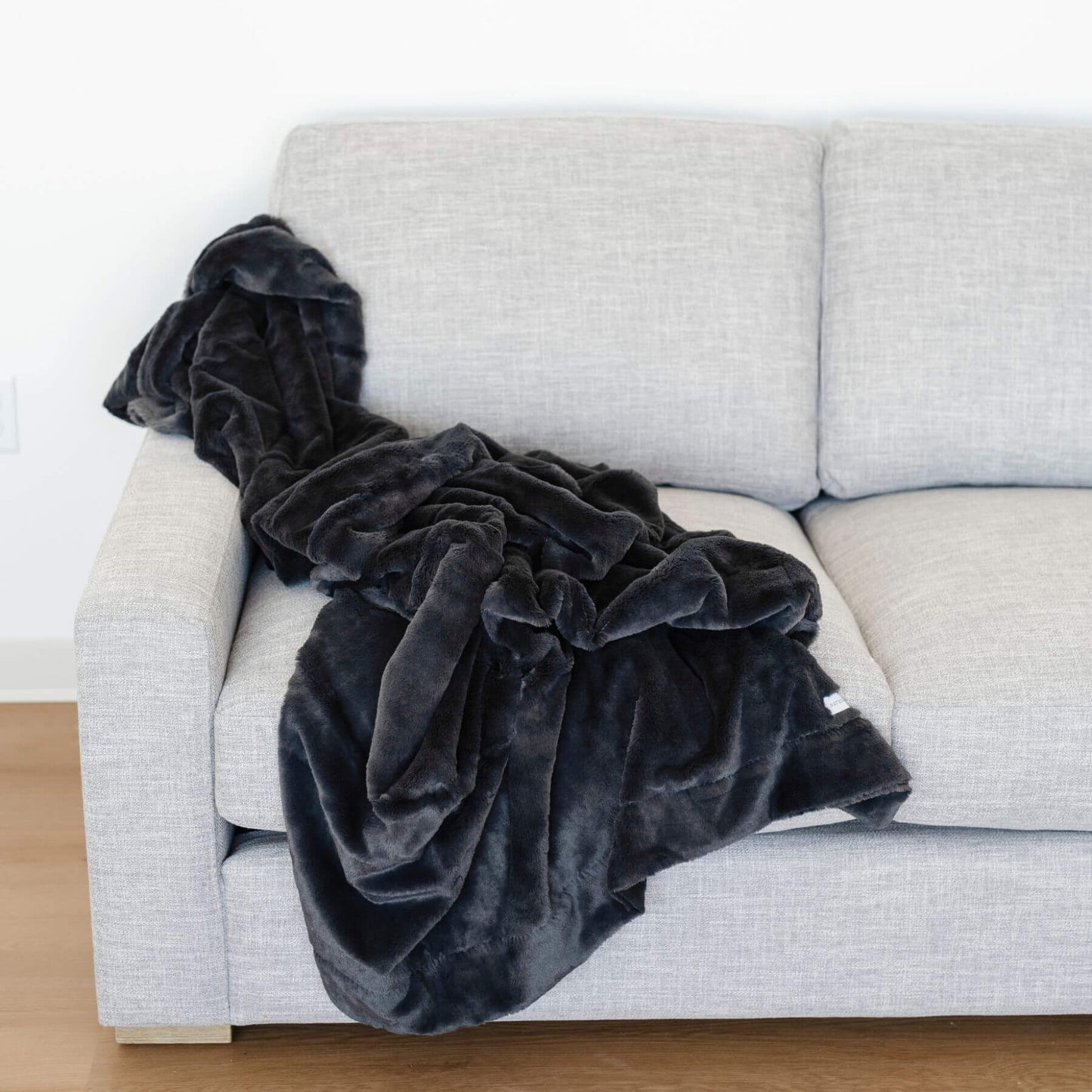 Saranoni Lush Throw Blanket Charcoal draped over a light gray sofa against a white wall.