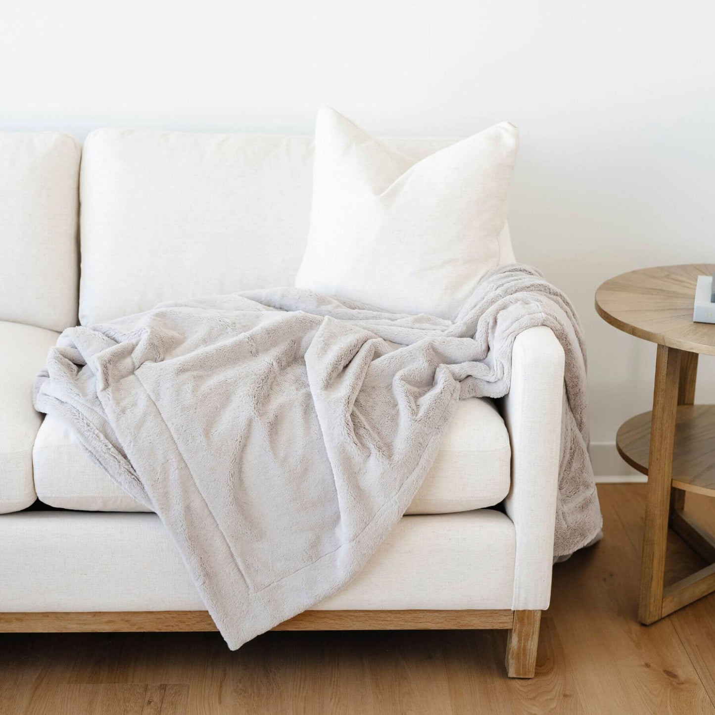 White sofa with a Saranoni Lush Throw Blanket Feather and pillows in a minimalistic room.