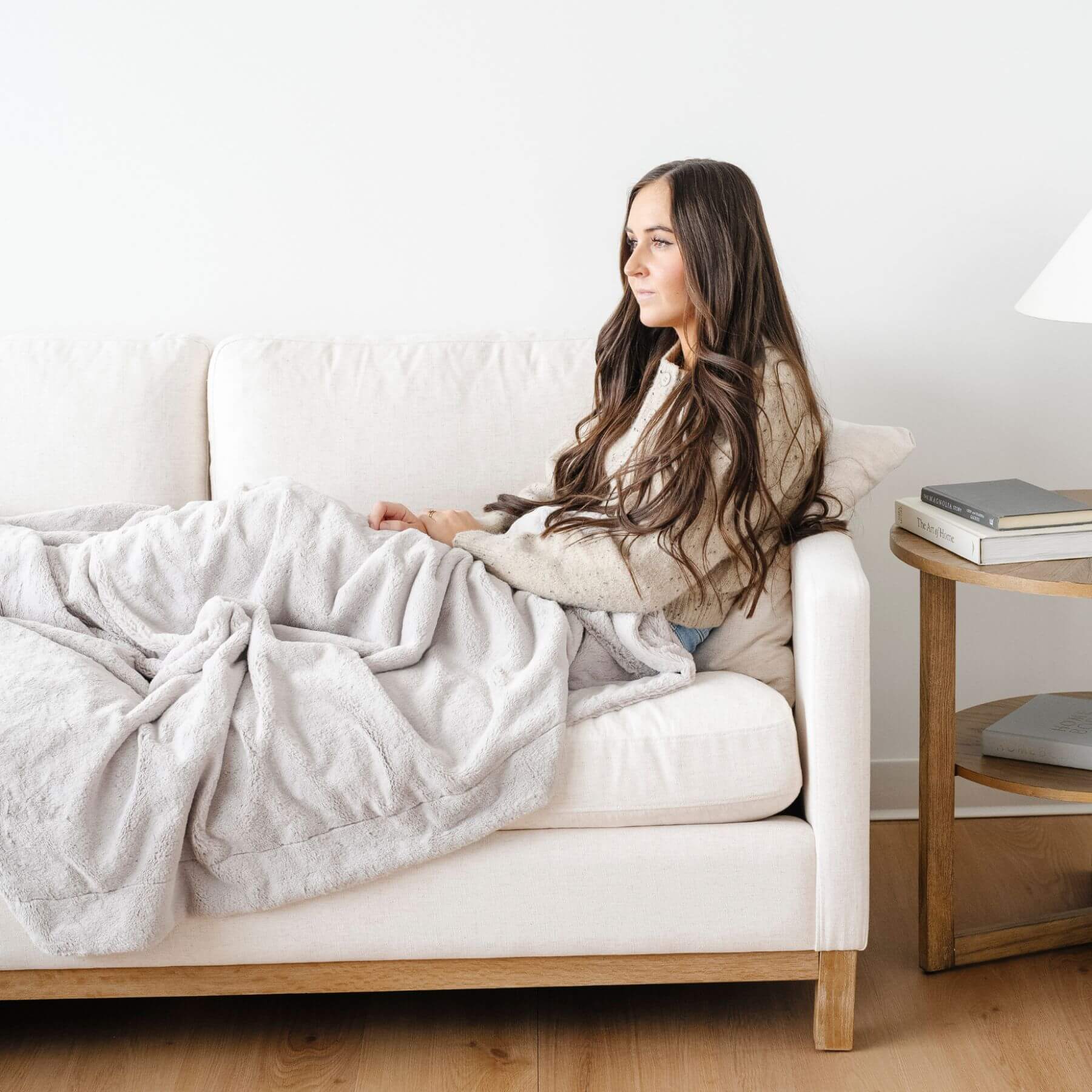 Woman sitting on a couch with a Saranoni Lush Throw Blanket Feather, looking at a laptop in a cozy living room.
