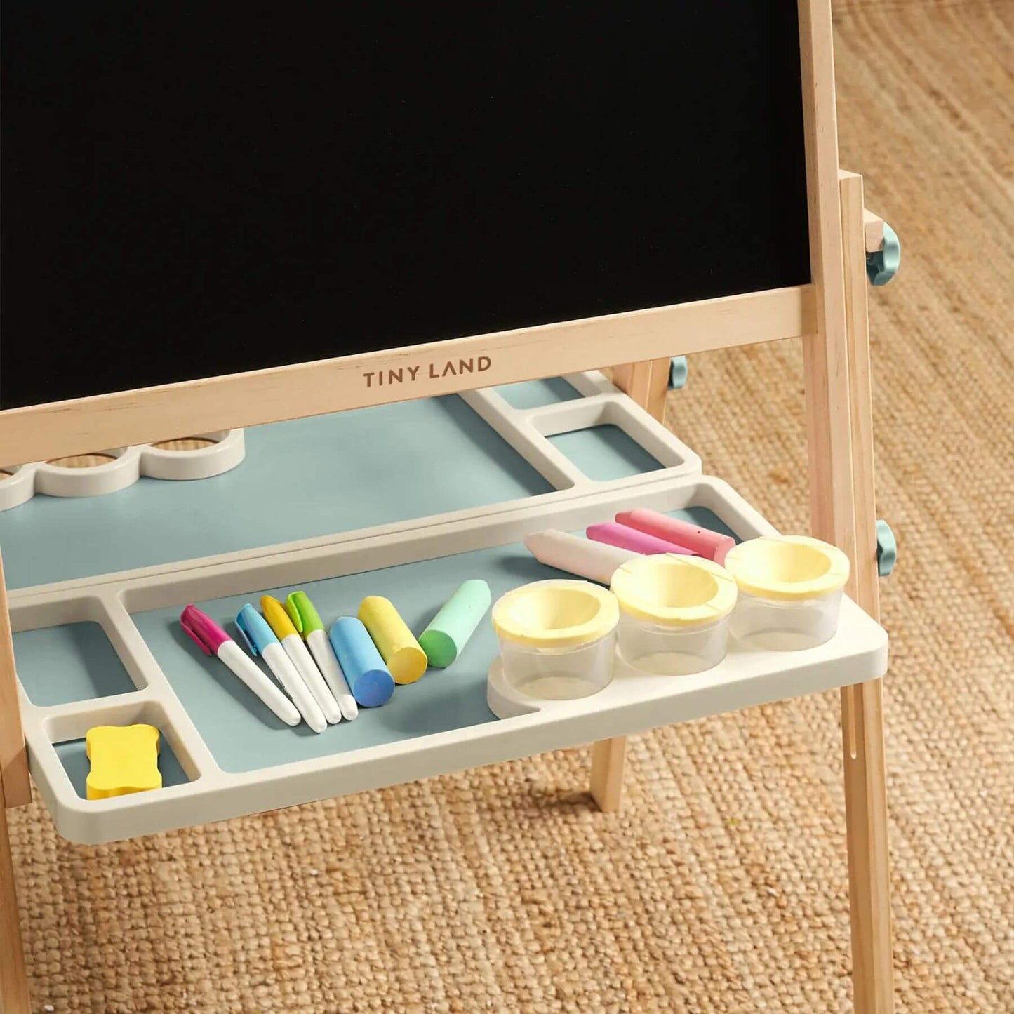 Children's art easel with blackboard surface and drawing tools on a wooden floor.