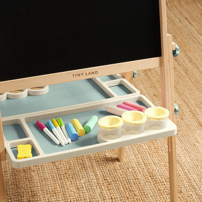 Children's art easel with blackboard surface and drawing tools on a wooden floor.
