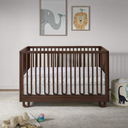 Soho Baby Meridian Island Crib - Cognac, styled in a nursery setting with a white mattress, patterned sheet, framed wall art, and a toy basket.