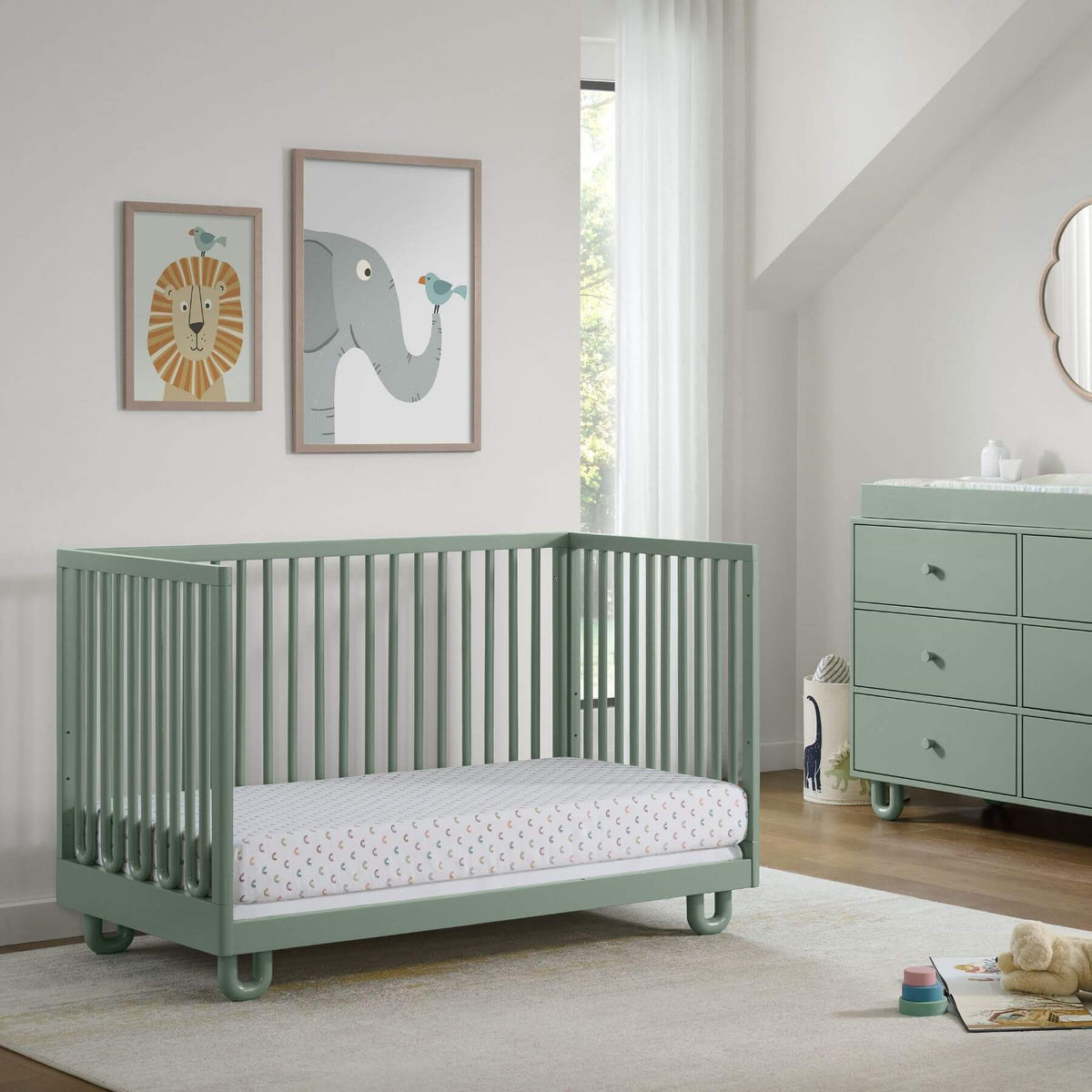 Soho Baby Meridian Island Crib - Olive Green with a mattress, shown in a styled nursery room with a matching dresser, framed animal art, and a window.
