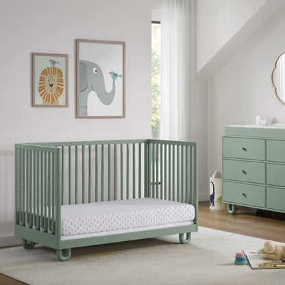 Soho Baby Meridian Island Crib - Olive Green with a mattress, shown in a styled nursery room with a matching dresser, framed animal art, and a window.