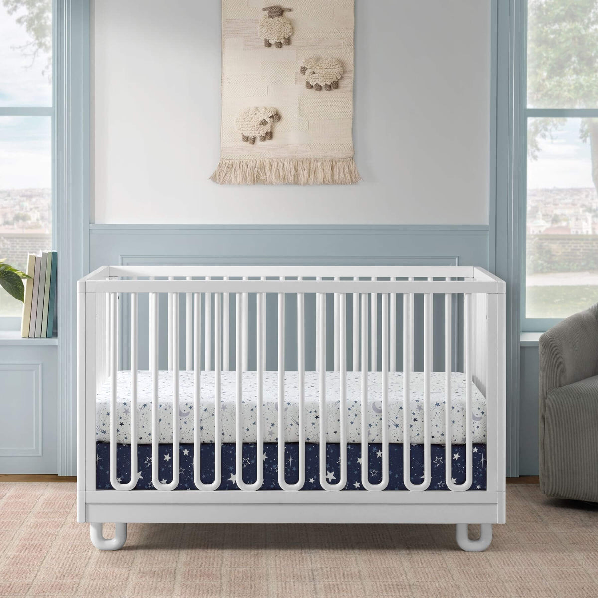 Soho Baby Meridian Island Crib - White and bedding, styled in a nursery with light blue wainscoting and windows.