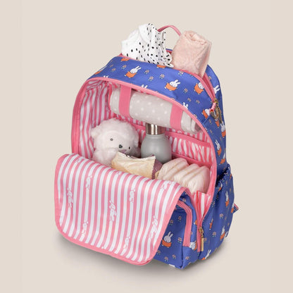 Miffy Flower Fields Zealous Diaper Bag Backpack - Blue & Orange filled with baby essentials, including a white teddy bear, a bottle, and folded cloth diapers, shown on a solid beige background.