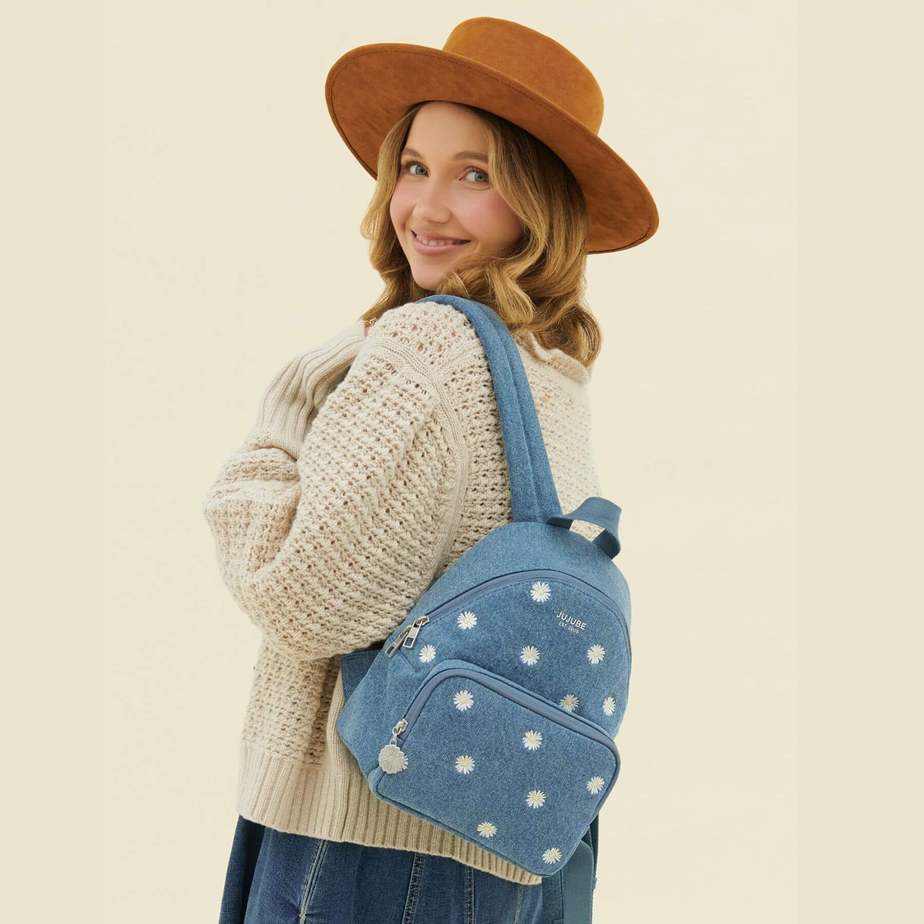 Woman wearing JuJuBe Everyday Mini Backpack - Denim & Daisies on a beige background