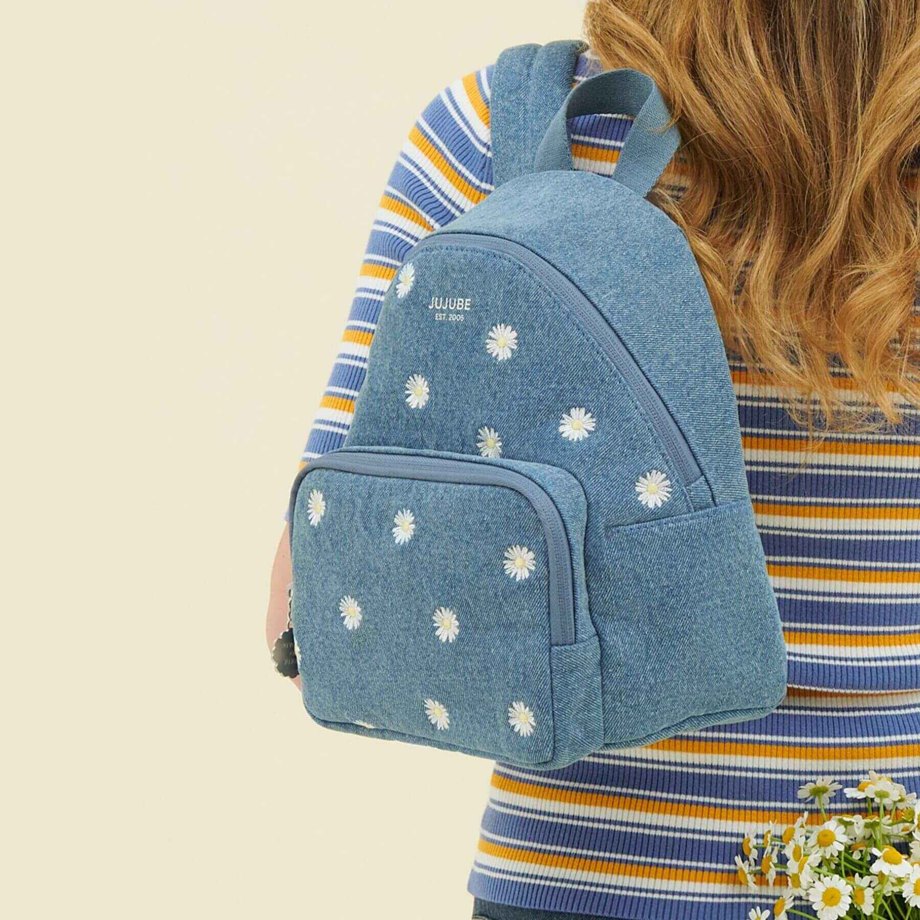 Person wearing JuJuBe Everyday Mini Backpack - Denim & Daisies on a beige background