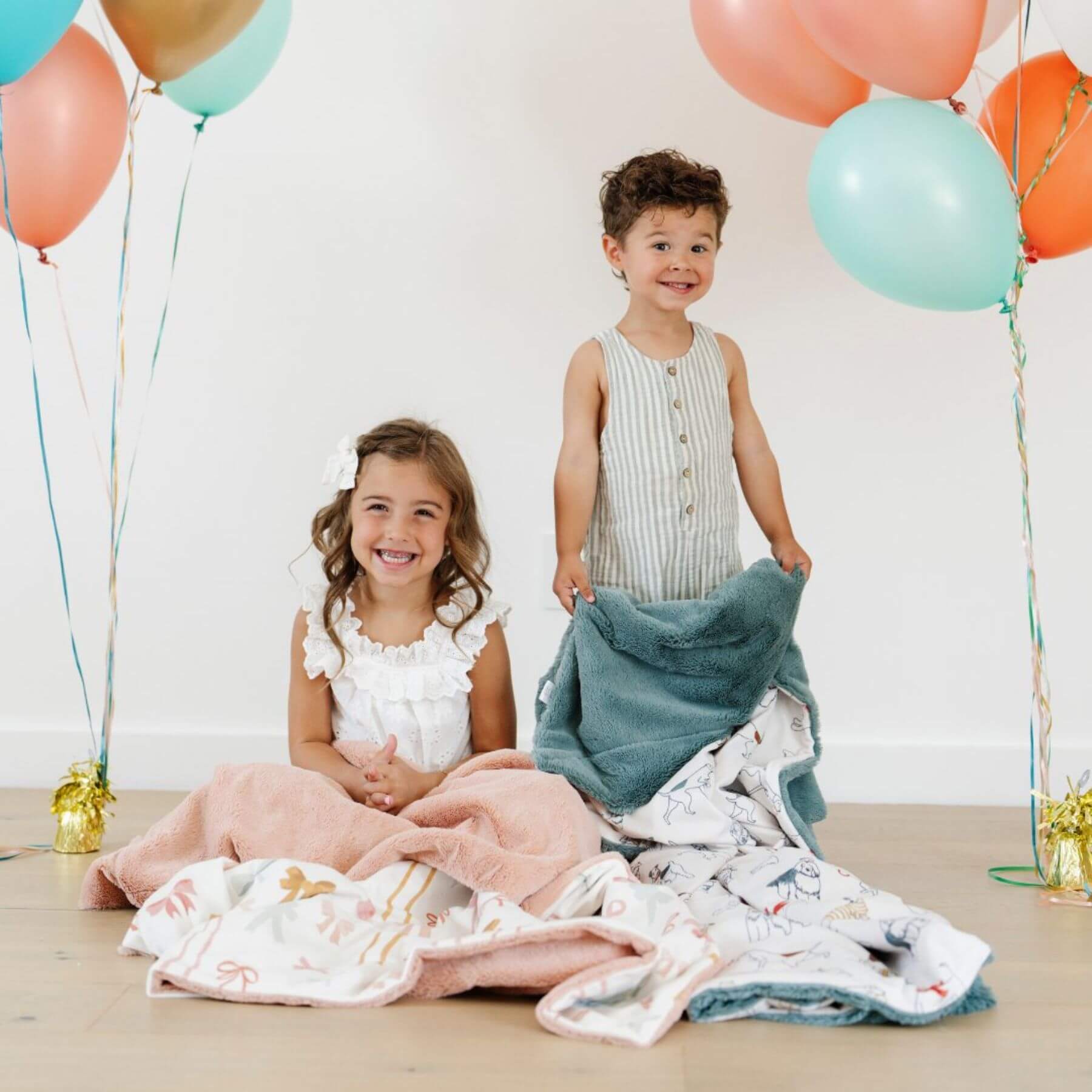 Two children surrounded by colorful balloons and Saranoni Minky/Lush Toddler Blanket on a light background