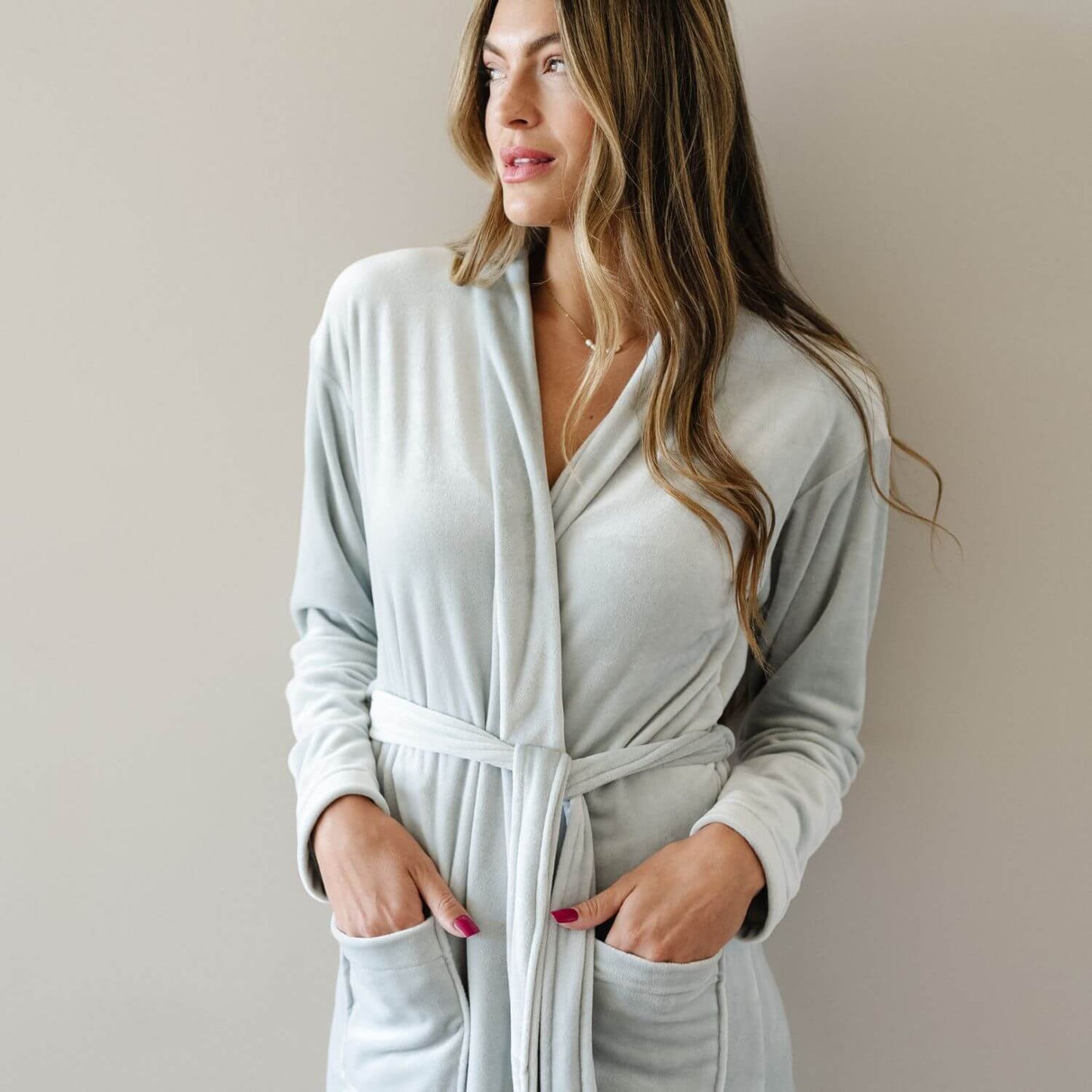A woman wearing Saranoni Minky Stretch Luxe Robe - Mirage, standing against a plain beige wall.