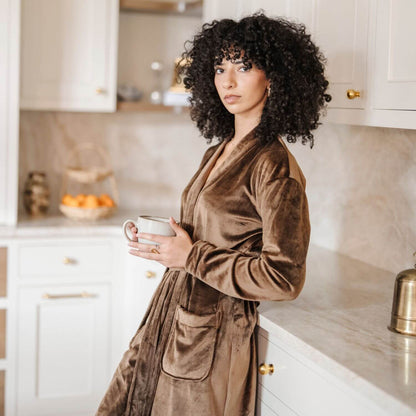 Woman in Saranoni Minky Stretch Luxe Robe - Mocha holding a mug in a kitchen.