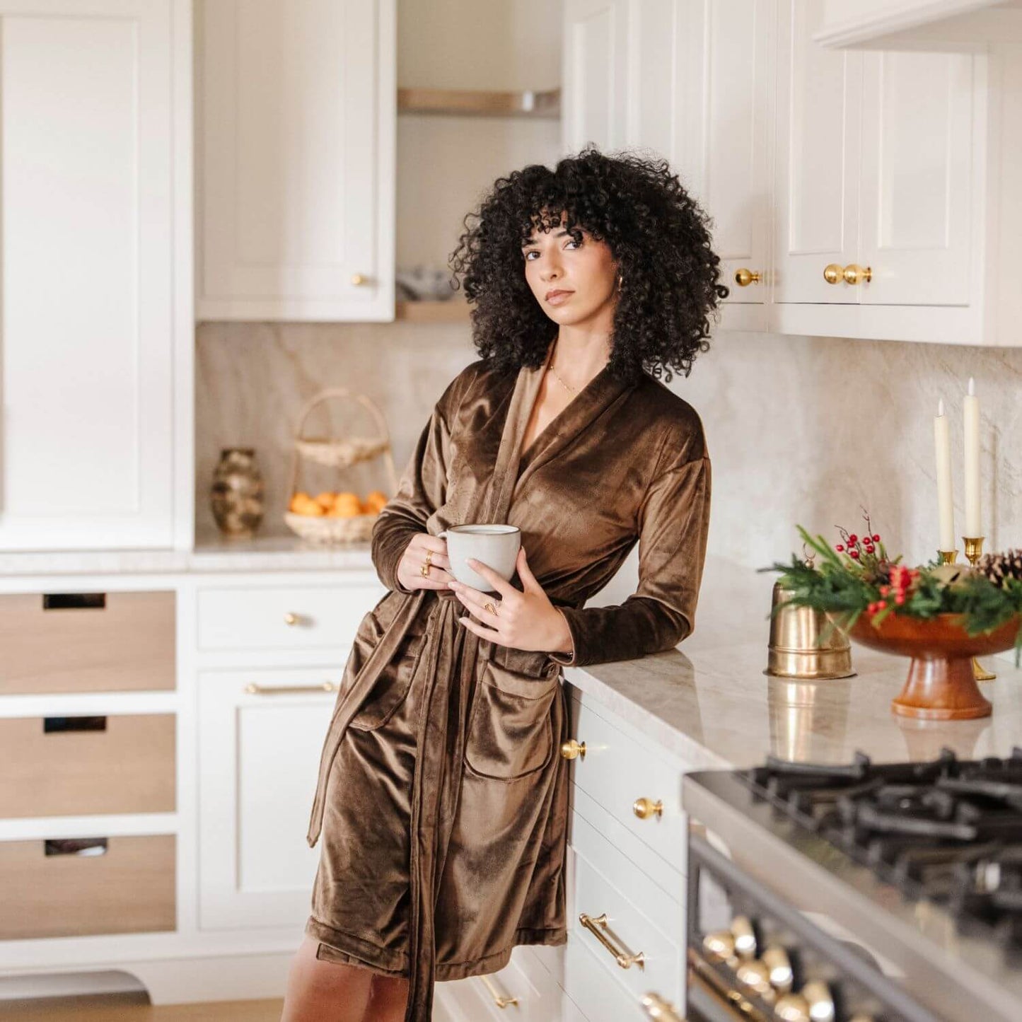 Woman in Saranoni Minky Stretch Luxe Robe - Mocha holding a mug in a kitchen.