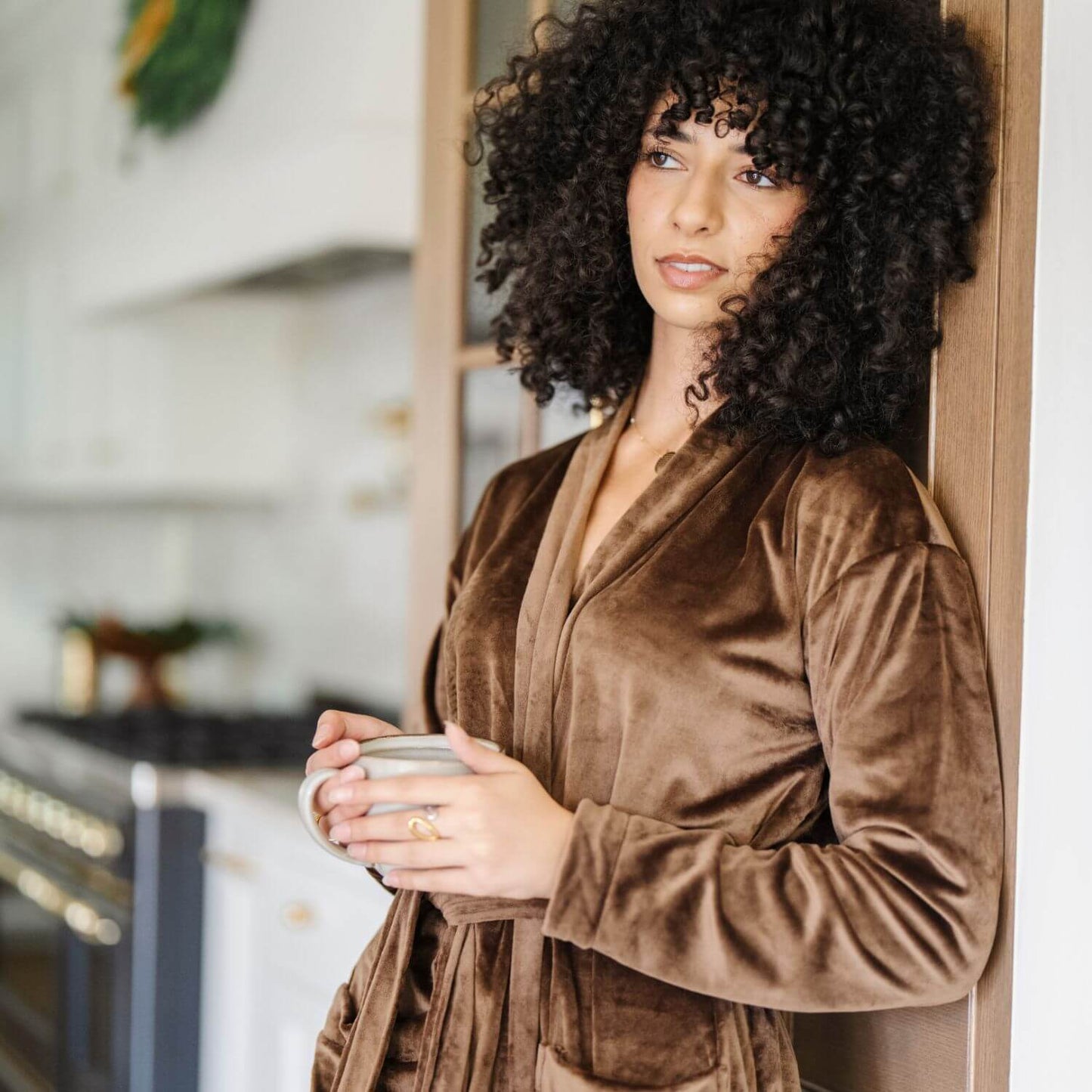 Woman in Saranoni Minky Stretch Luxe Robe - Mocha holding a mug in a kitchen setting