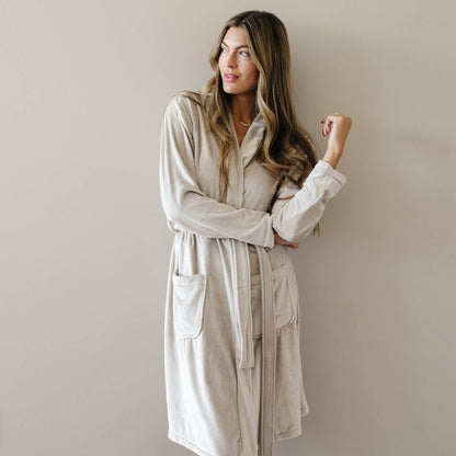 A woman wearing Saranoni Minky Stretch Luxe Robe - Sandshell, standing against a plain beige wall.