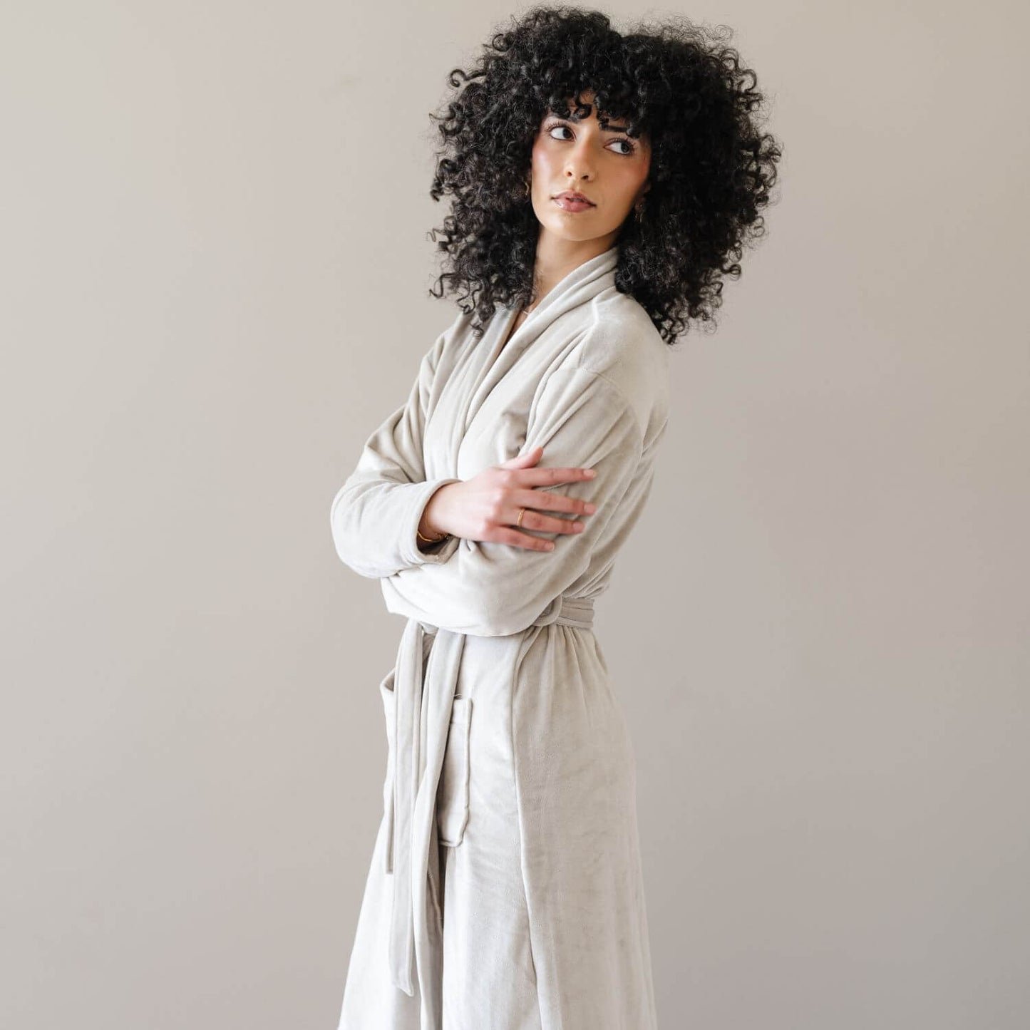 A model with wearing Saranoni Minky Stretch Luxe Robe - Sandshell, standing against a neutral beige background.