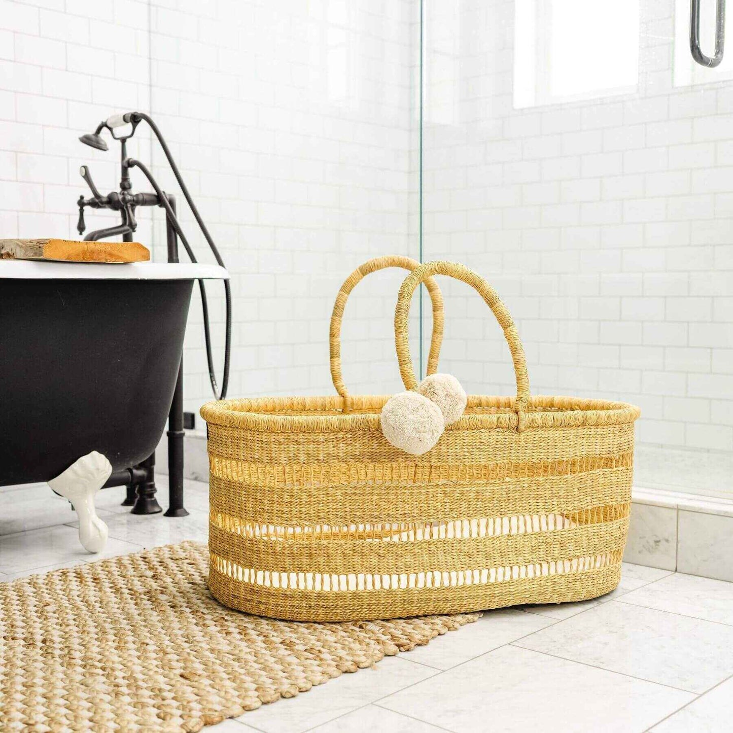 Modern Open Weave African Moses Basket Vegan Handle (No Hood) on a bathroom floor next to a black bathtub.