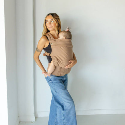 Woman holding a baby in Monroe x Coco Desert - Cotton Linen Baby Carrier against a white wall