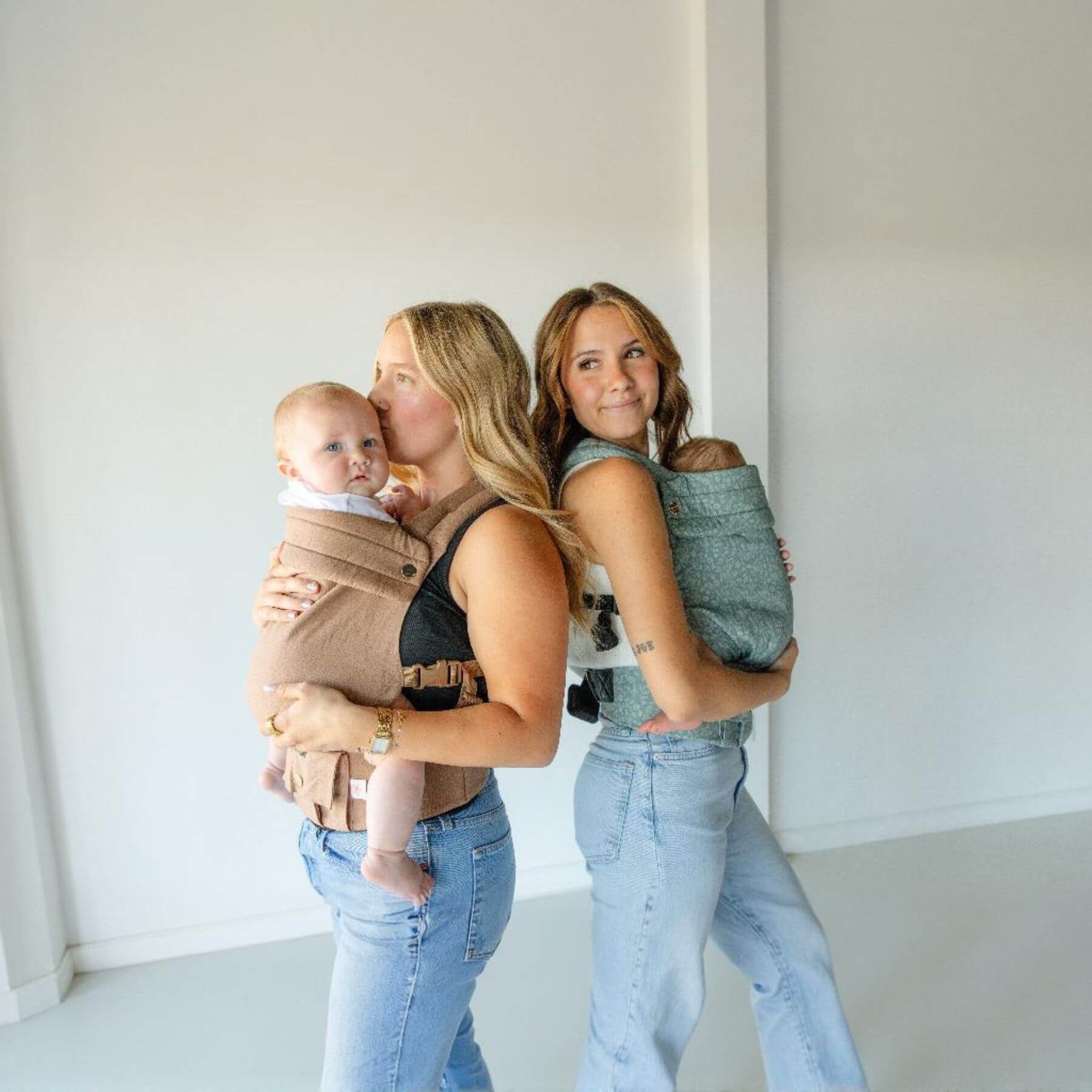 Two women standing side by side, each holding a baby in Monroe x Coco Desert - Cotton Linen Baby Carrier