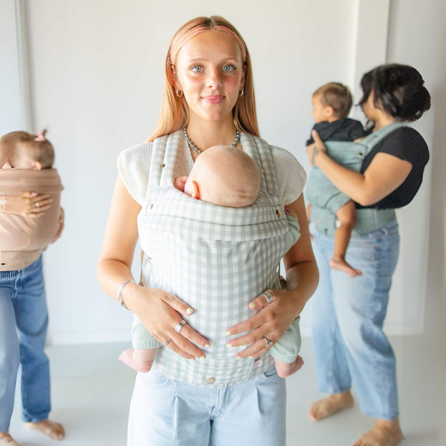 Two women holding babies in Monroe x Coco Gingham - Cotton Baby Carriers against a white background