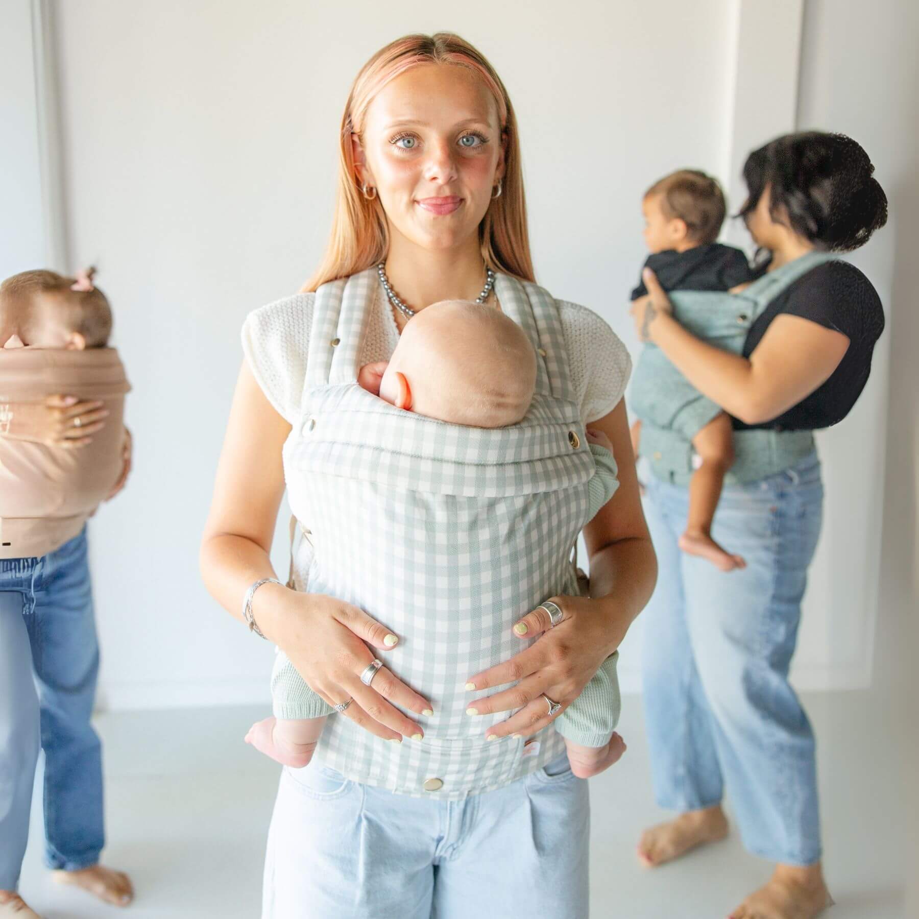Two women holding babies in Monroe x Coco Gingham - Cotton Baby Carriers against a white background