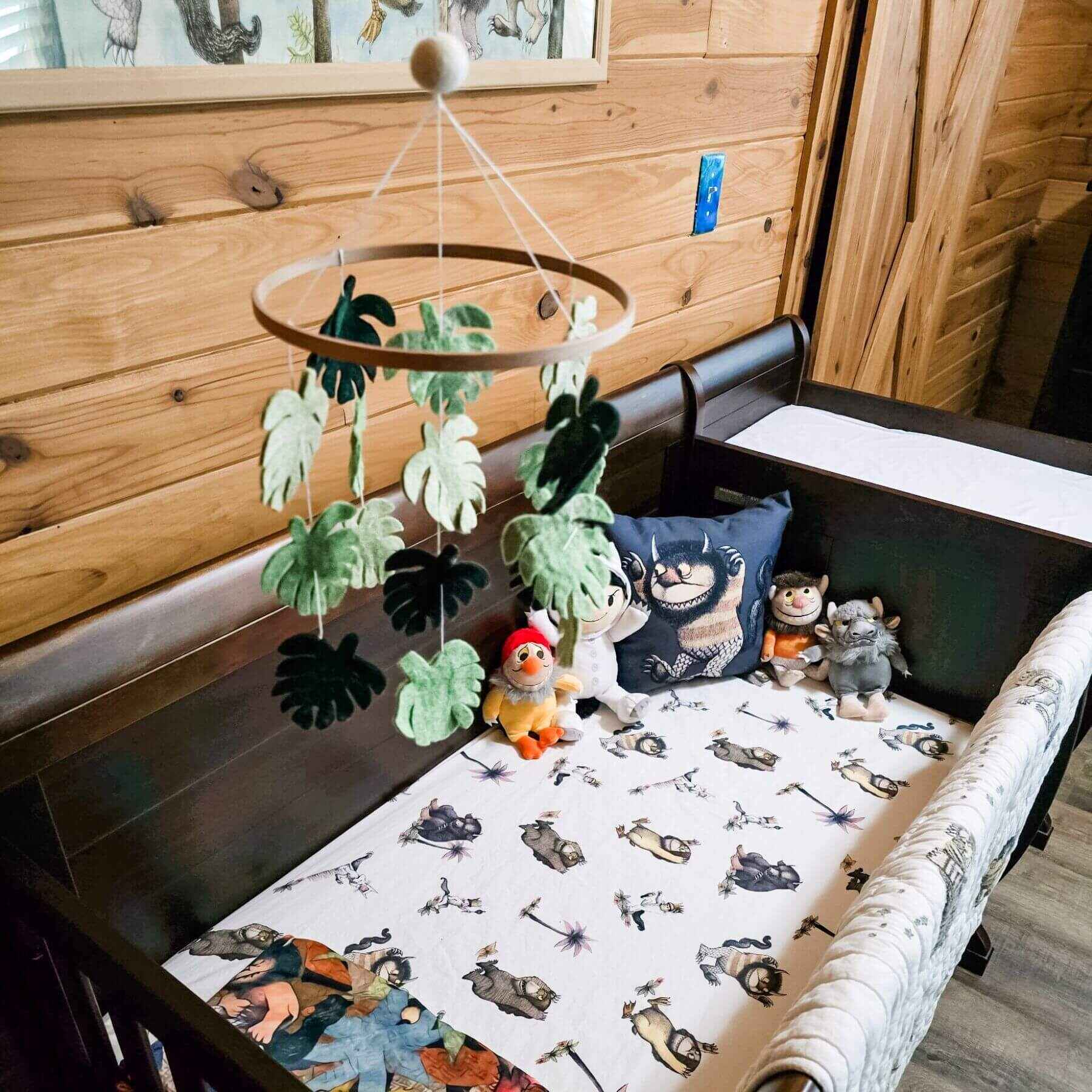 Baby crib with a mobile featuring leaves and plush toys, against a wooden wall.