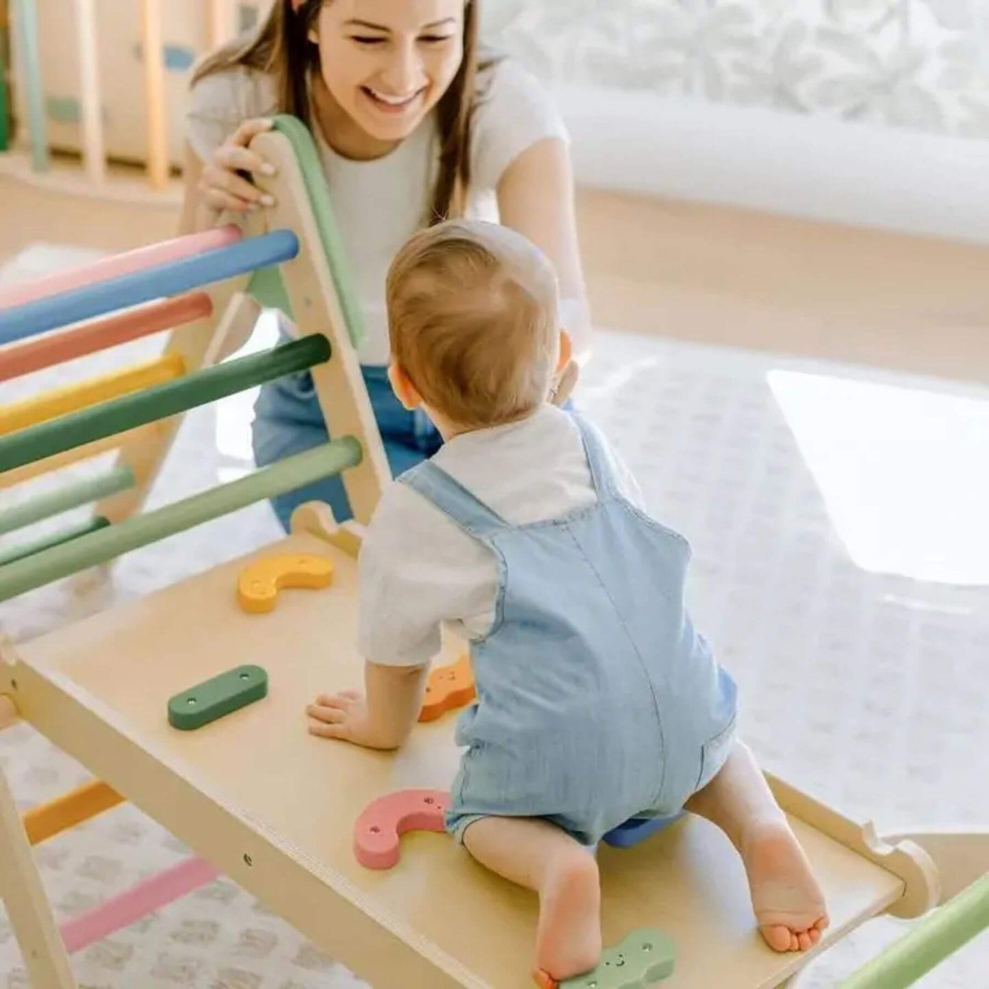 Baby playing with Tiny Land® 7-in-1 Morandi Pikler Triangle Set with a woman in the background.