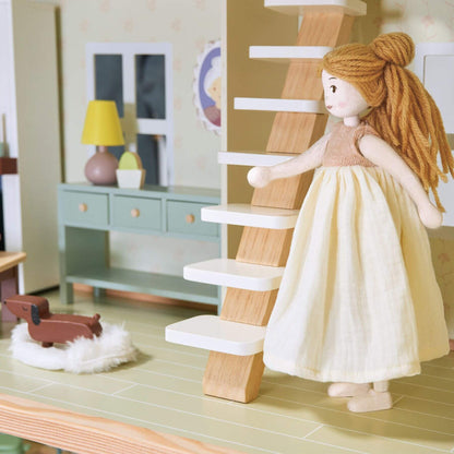 Dollhouse with a doll in a yellow dress standing on a staircase