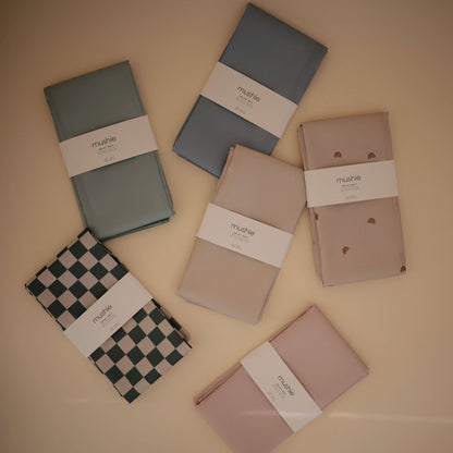 Six folded Mushie Splat Mats, arranged on a warm beige background.