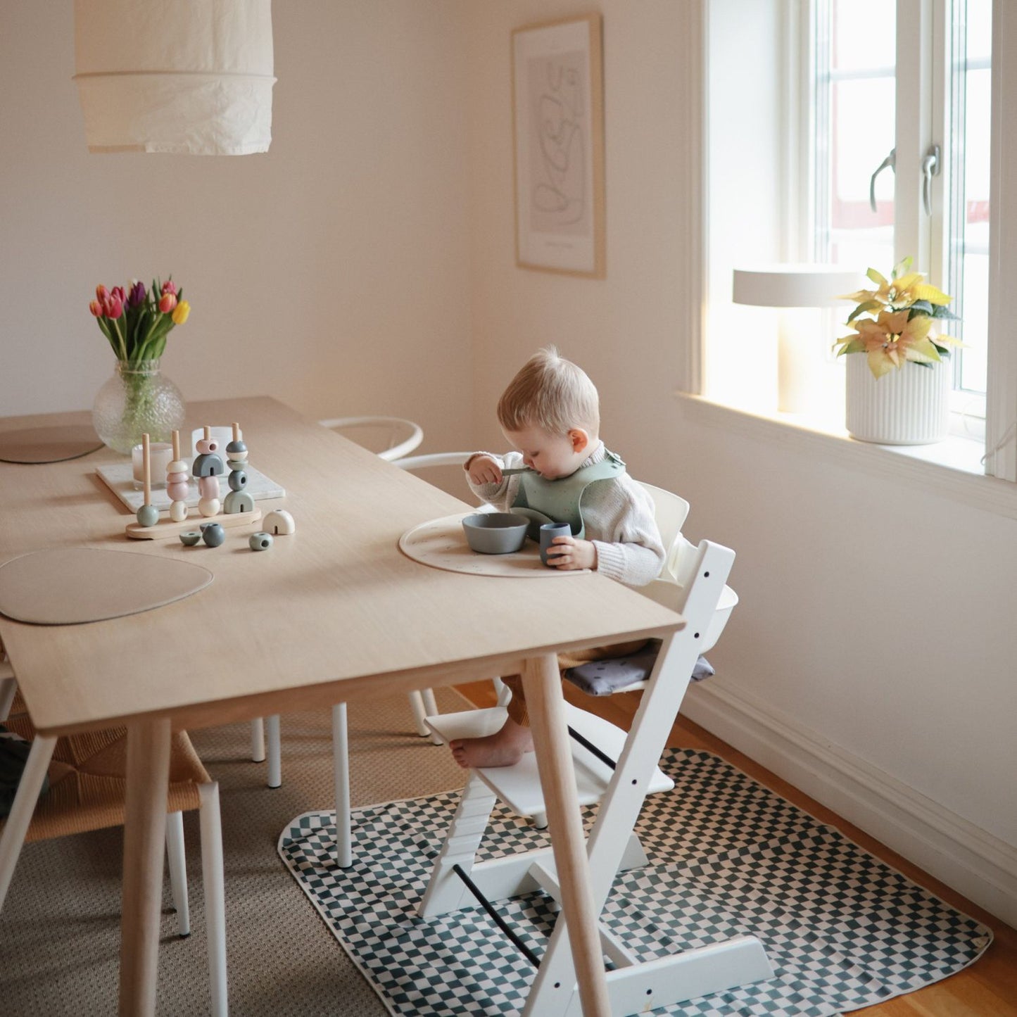 Child sitting at a table in a bright room with toys and a window in the background