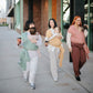 Three women walking on a sidewalk, each carrying a baby in Mushie Baby Wrap.