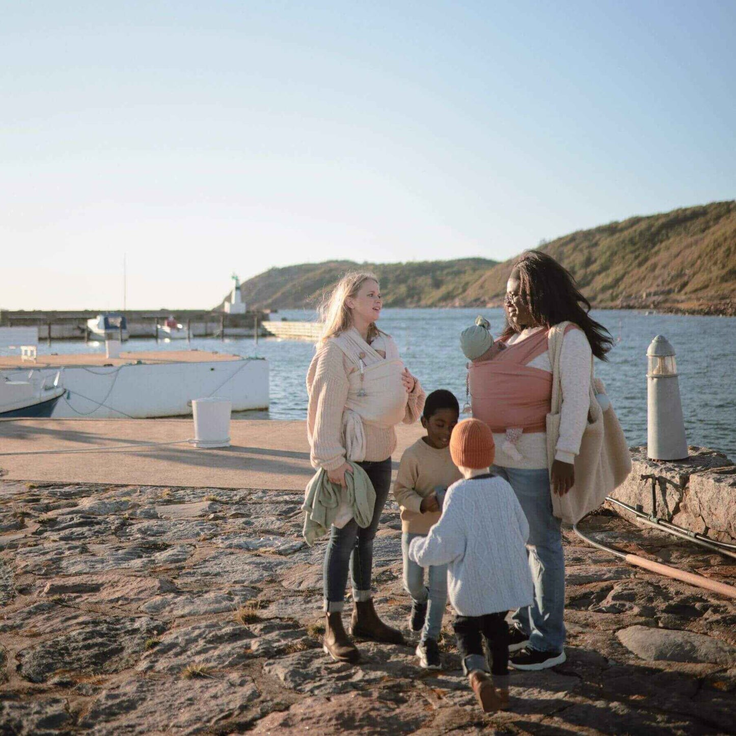Family of four standing on a rocky dock by the water with boats in the background.