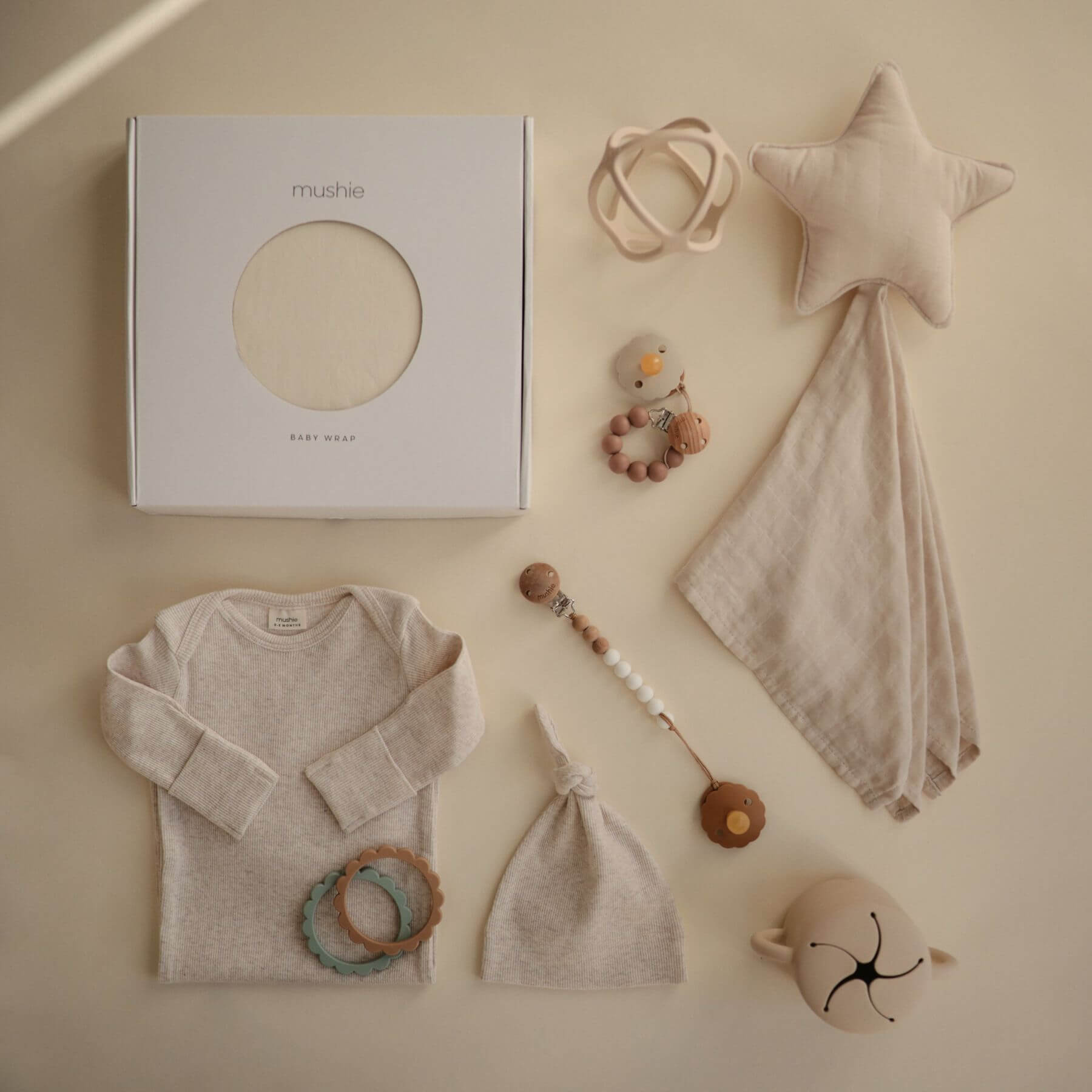 Collection of baby items including a onesie, hat, wrap, and toys on a beige background