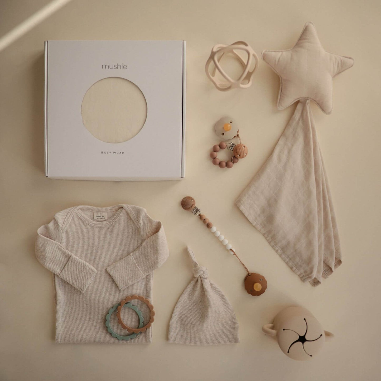 Collection of baby items including a onesie, hat, wrap, and toys on a beige background