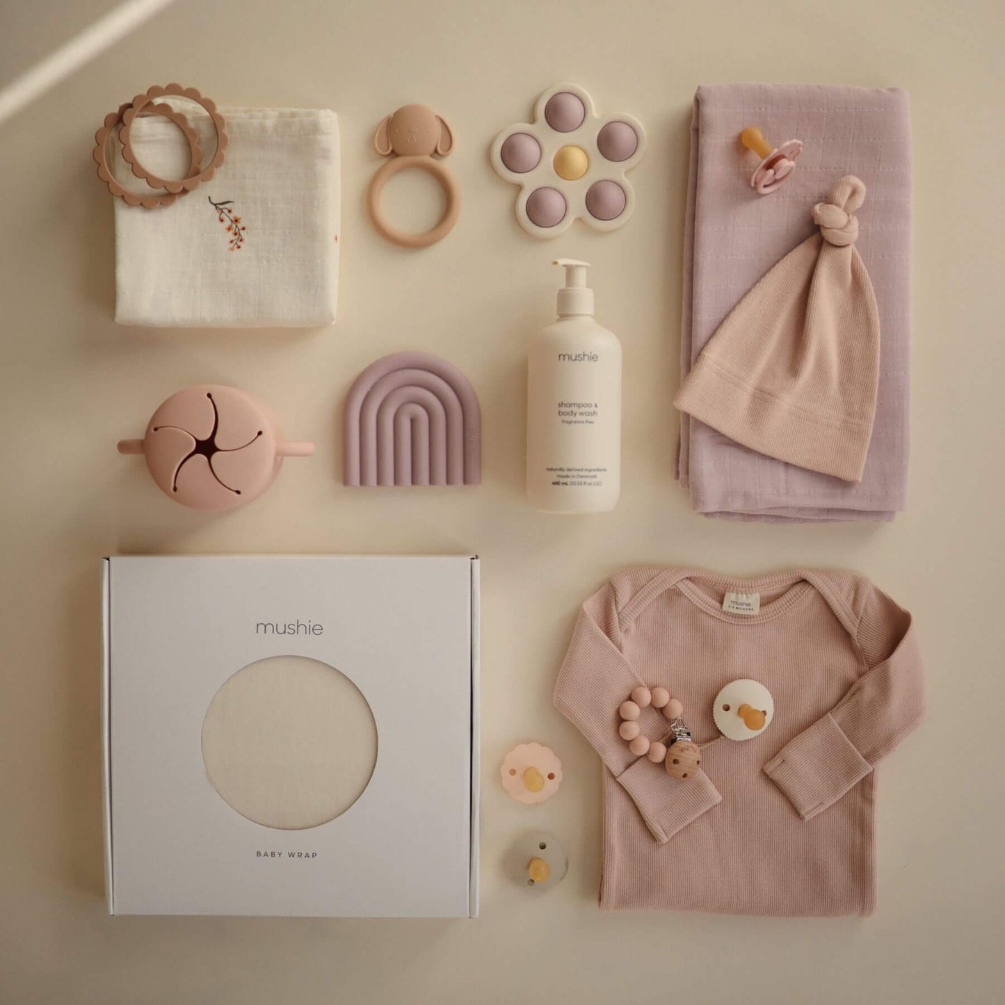 Collection of baby products including a onesie, toys, wrap, and a bottle on a beige background