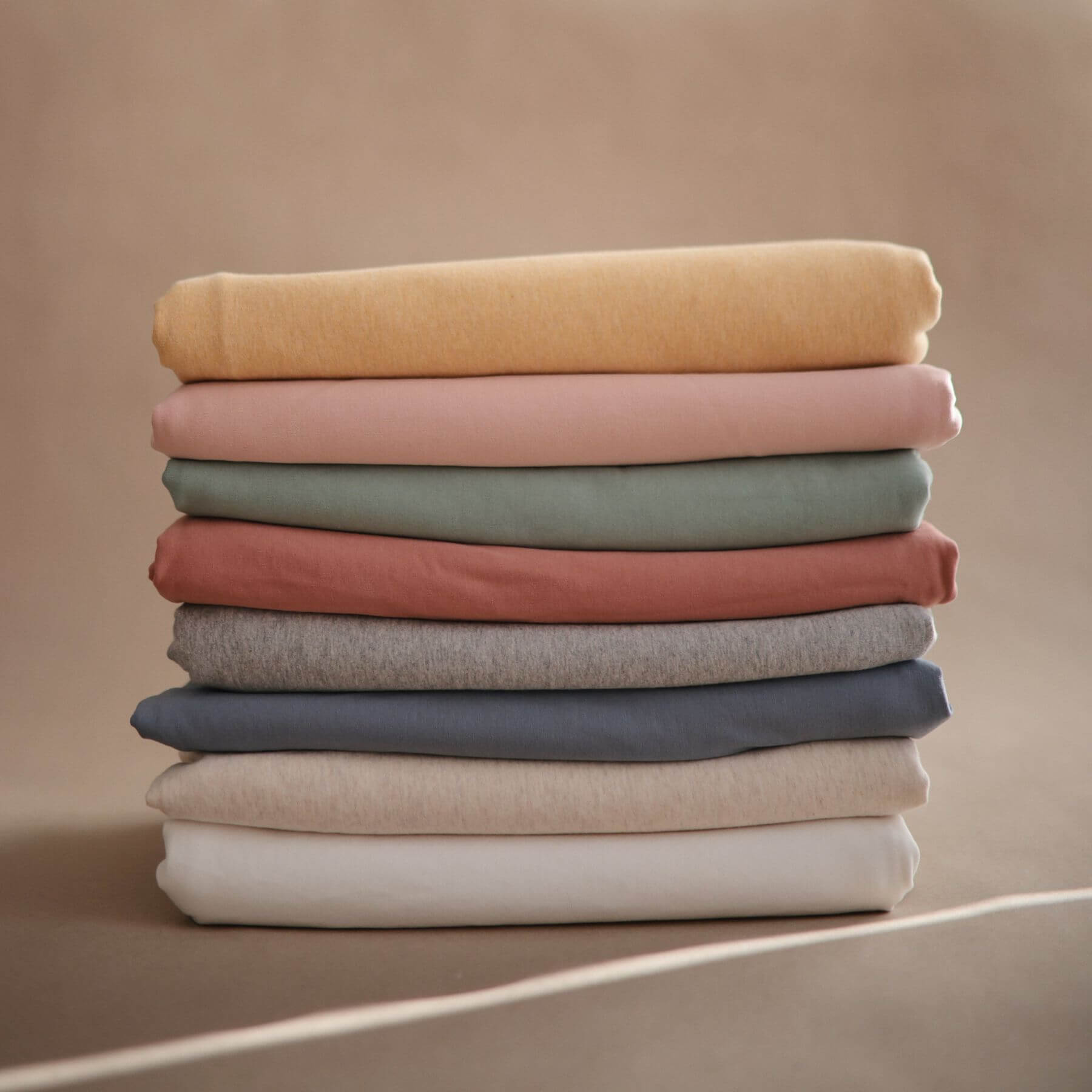 Stack of folded Mushie Baby Wrap in various colors on a beige background