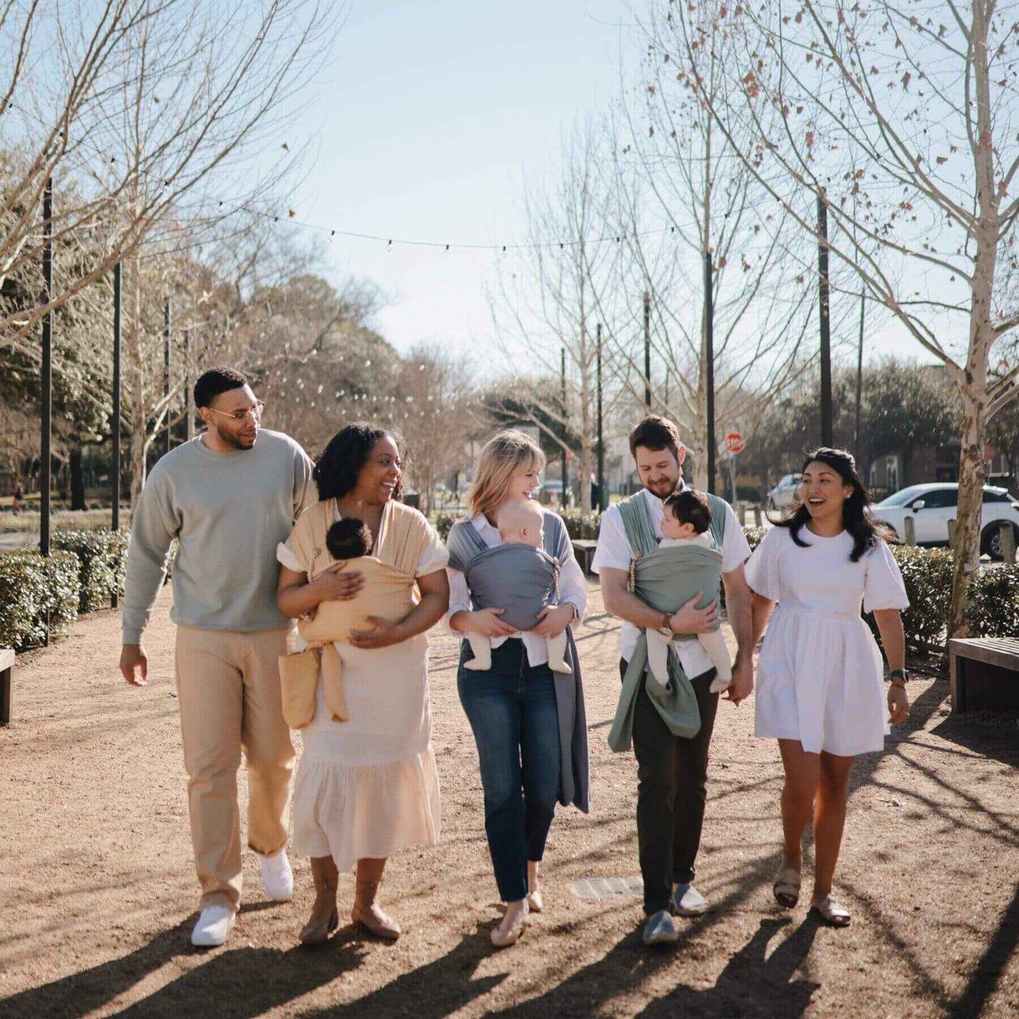Five people walking outdoors on a path with trees and cars in the background
