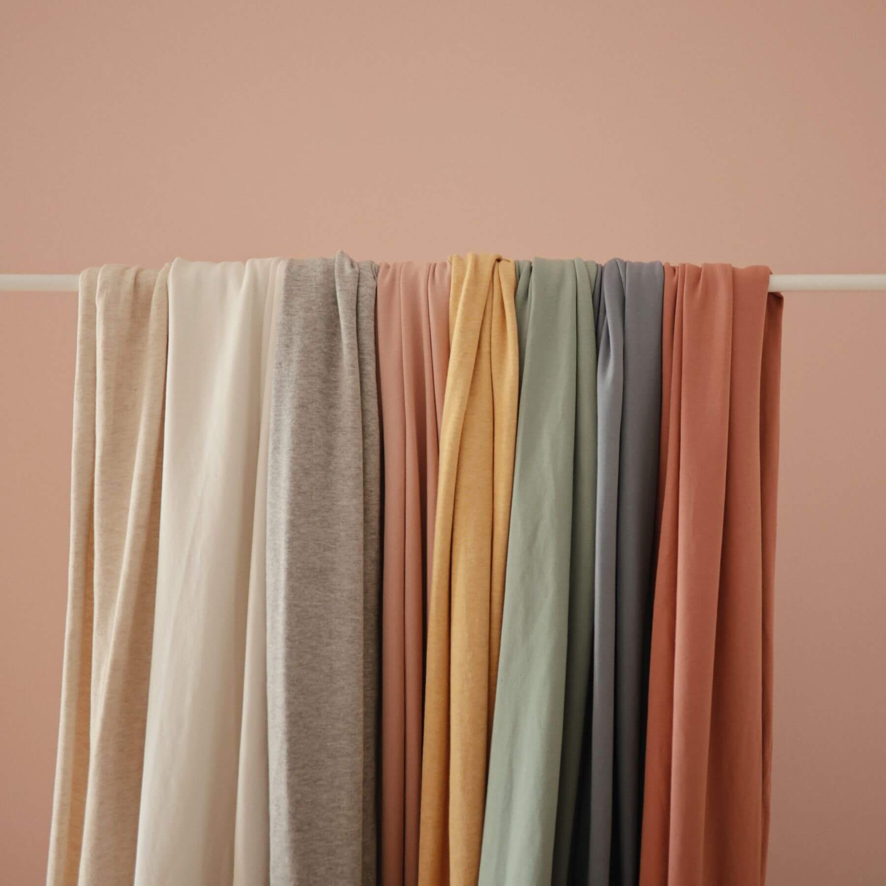 Stack of Mushie Baby Wraps on a white rod against a pink background