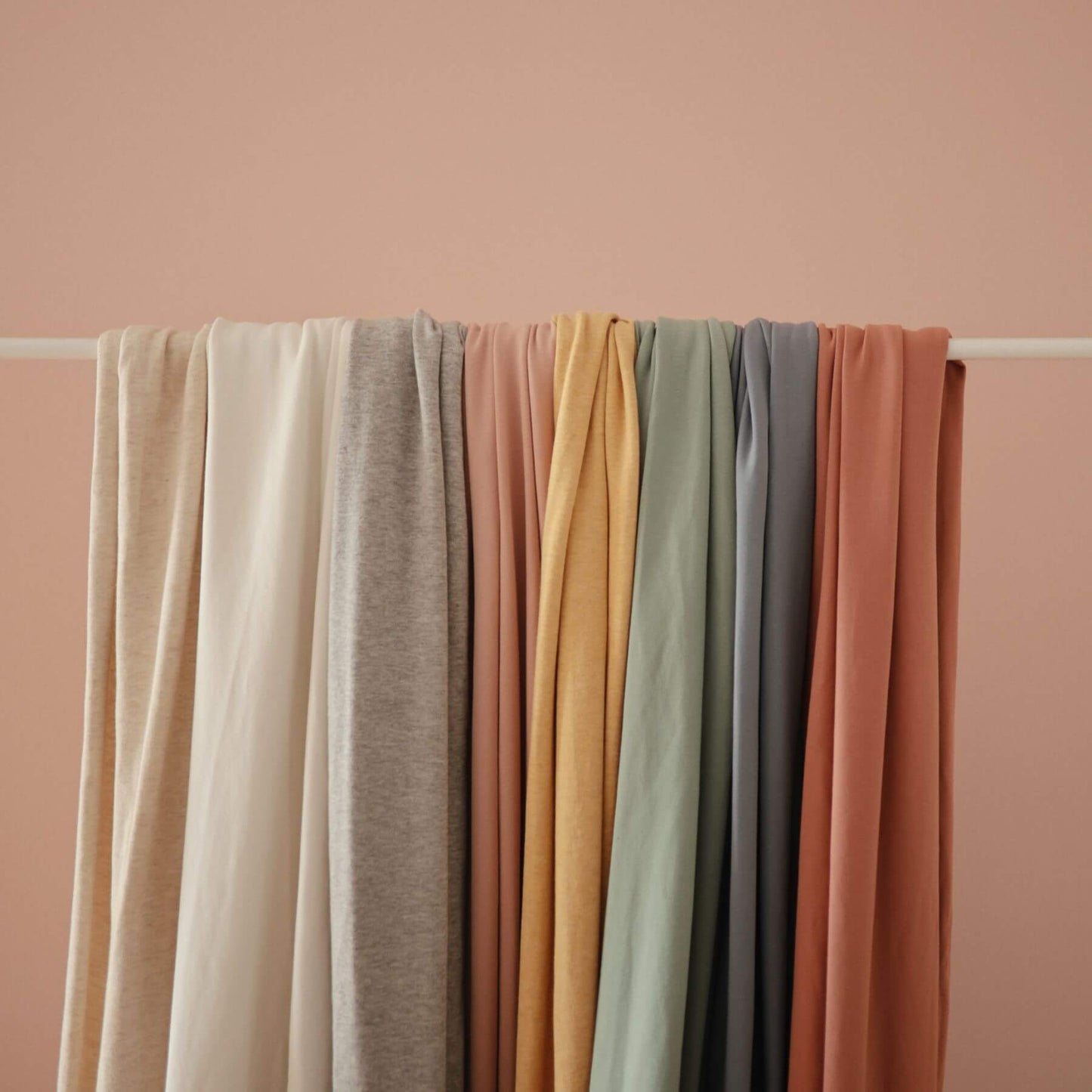 Stack of Mushie Baby Wraps on a white rod against a pink background