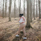Person standing in a forest holding a baby in Mushie Baby Wrap and beige pants.